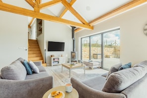 Ein geräumiges Wohnzimmer mit hoher Decke, Kamin, Fernseher und Blick ins Freie.