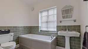 Un baño con inodoro, bañera, lavamanos y ventana con persianas.