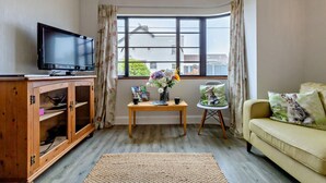 Una sala de estar con televisor, aparador de madera, mesa con flores y un sofá con cojines.