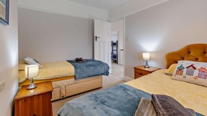 Un dormitorio con dos camas, una mesita de noche con lámpara, un armario y una puerta que da a otra habitación.