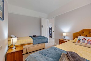 A bedroom with two beds, a bedside table with a lamp, a wardrobe, and a door leading to another room. - 3 Bed in Overstrand (oc-g29294) (Overstrand)
