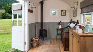 Ein gemütliches Blockhauss-Interieur mit Kaminofen, einem Essbereich mit Tisch und Stühlen sowie Blick auf die umliegende Natur.