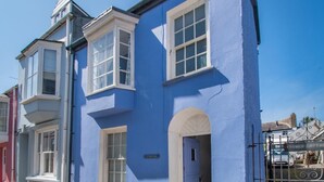 Un bâtiment à deux étages avec une façade bleue, des encadrements de fenêtres blancs et un petit porche.