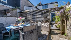 Un espace patio aménagé avec des meubles en osier, une table dressée avec de la nourriture et des boissons, et une pergola en bois ornée de plantes grimpantes.
