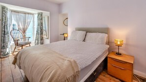 Une chambre à coucher avec un grand lit, deux lampes de chevet, une table de chevet en bois, une chaise et une fenêtre avec des rideaux.