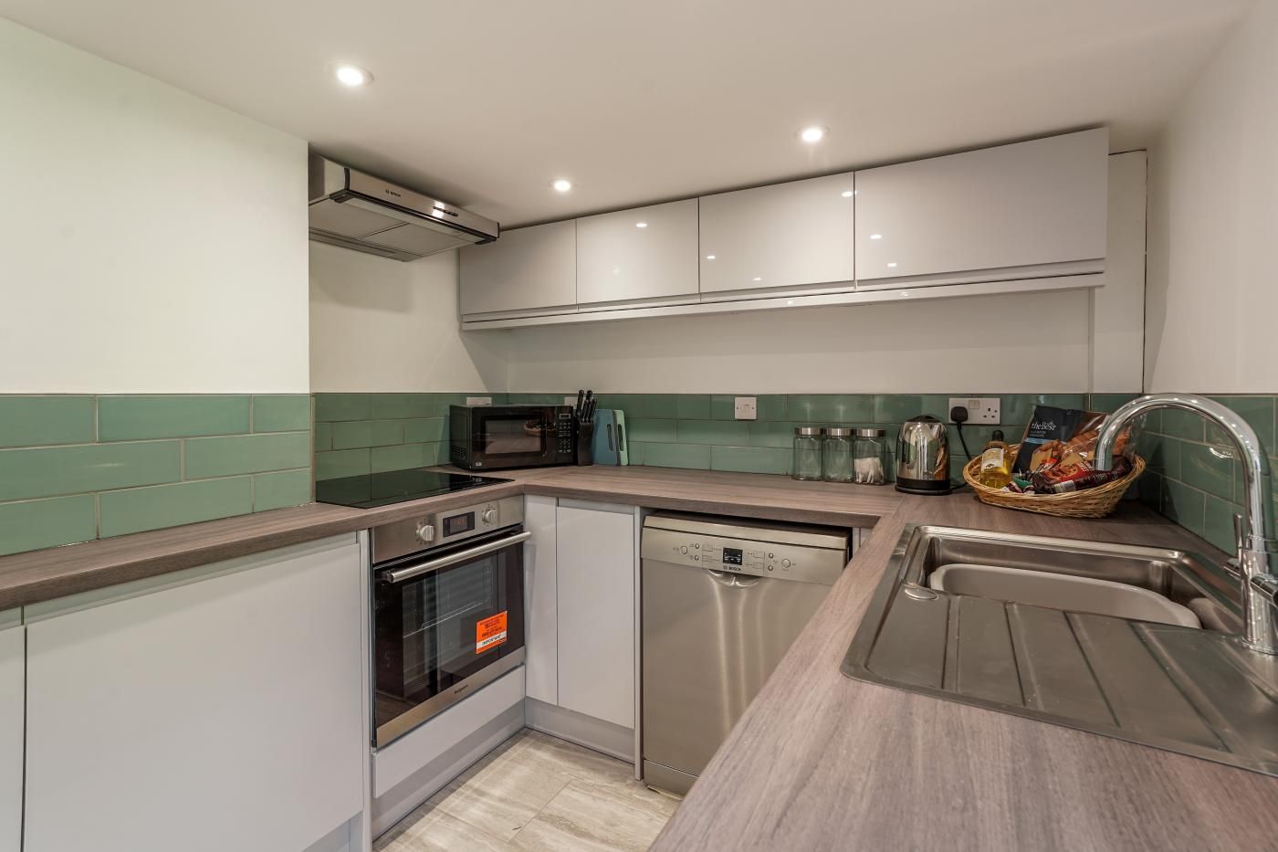 A modern kitchen with a built-in oven, microwave, dishwasher, and a stainless steel sink.