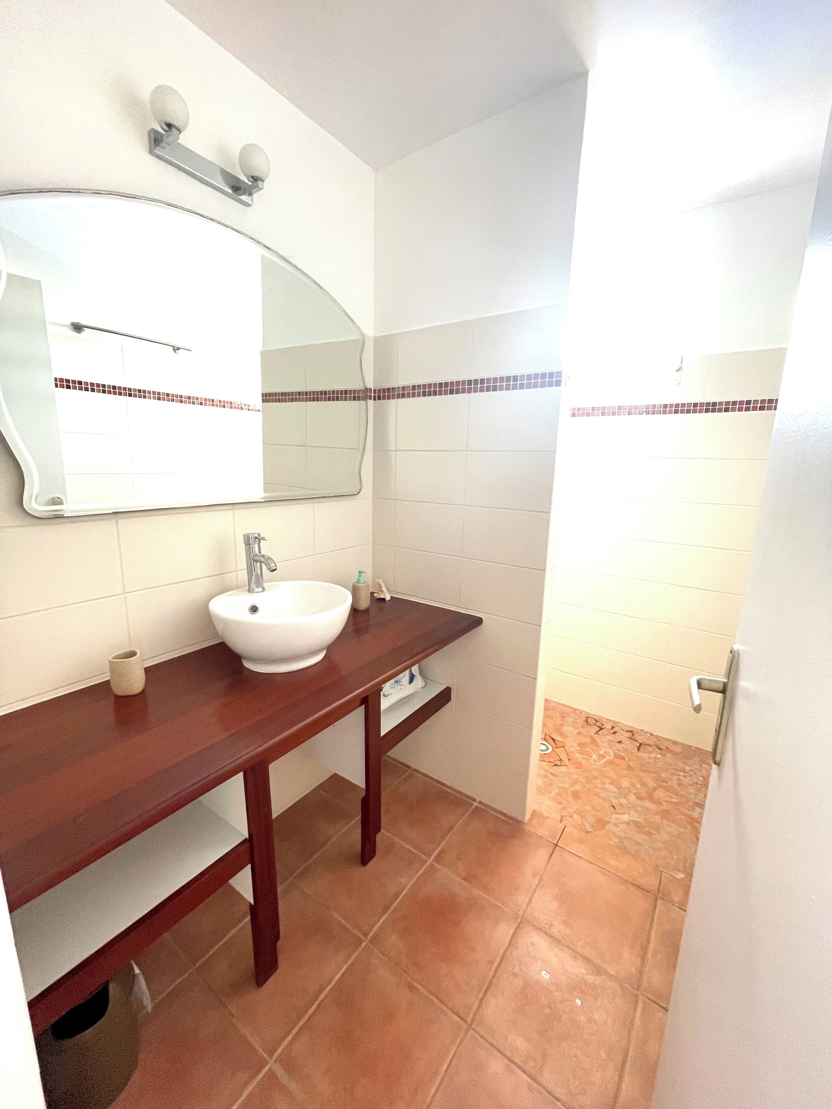 A bathroom with a white sink, a wooden vanity, a mirror, and a tiled floor.