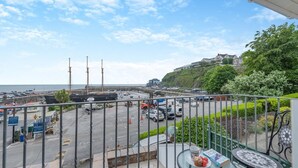 En balkon med udsigt over en lystbådehavn, et stort skib og en bakke med bygninger.