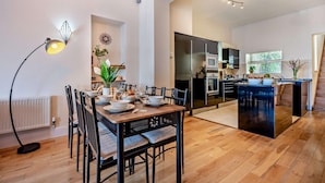 Una cucina moderna con isola centrale, zona pranzo con tavolo apparecchiato per quattro e una scala che conduce a un piano superiore.