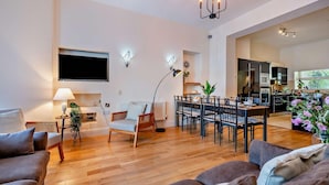 Un soggiorno moderno con zona pranzo, televisore a schermo piatto e cucina sullo sfondo.