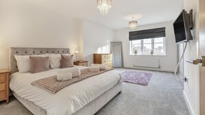 A bedroom with a large bed, bedside tables, a dresser, a TV mounted on the wall, and a window with a view.