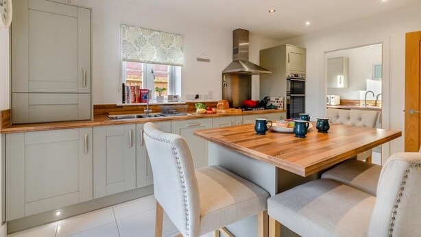 A modern kitchen with light grey cabinets, a wooden countertop, and a dining table with chairs.