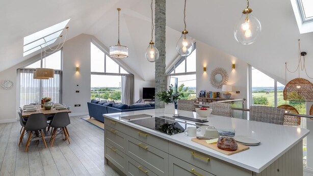 Une cuisine spacieuse dotée d’un grand îlot central, de luminaires suspendus modernes et offrant une vue sur l’extérieur.