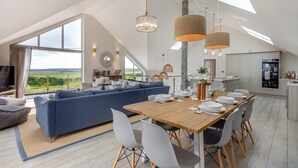 Un salon moderne doté d’un grand canapé, d’une table à manger et de chaises. De grandes fenêtres offrent une vue sur l’extérieur.