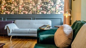 A room with a grey sofa, a green armchair, a bookshelf, and a floral wallpaper. - 6 Bed in Alnwick (oc-b29336) (Alnwick)