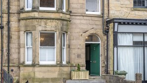 A stone building with a green door, multiple windows, and a small garden area. - 6 Bed in Alnwick (oc-b29336) (Alnwick)