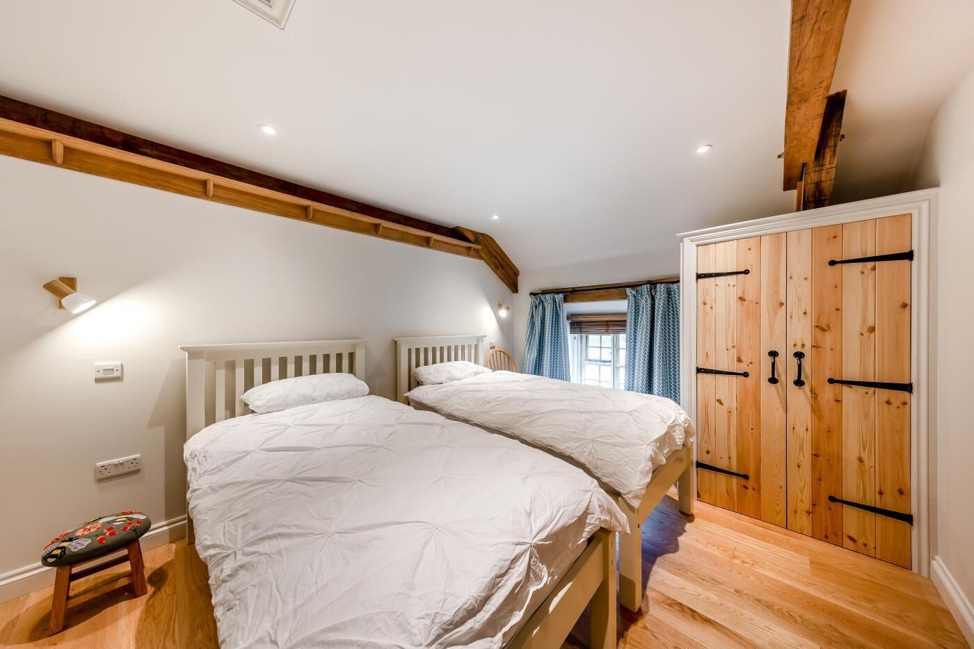 Une chambre avec deux lits, des poutres en bois, une armoire et une fenêtre avec des rideaux.