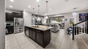 Une cuisine moderne dotée d’un grand îlot central, de meubles de couleur sombre, d’appareils électroménagers en acier inoxydable et de luminaires suspendus.