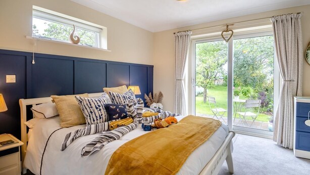 Quarto com cama grande, janela com cortinas, vista para o jardim e mesa de cabeceira com abajur.