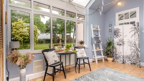 Uma estufa com vista para um jardim, uma mesa com cadeiras e uma estante escada.