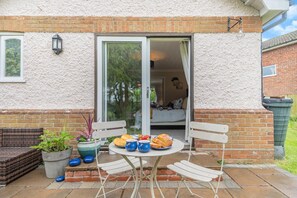 Une terrasse avec une table dressée pour deux personnes, un canapé en osier et une plante en pot.