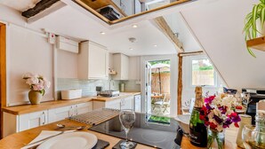 A modern kitchen with white cabinets, a wooden countertop, and a dining area with a table set for two. - 1 Bed in Chilham (oc-t29281) (Chilham)