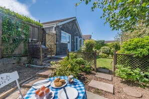 A stone house with a wooden fence, a garden with stepping stones, and a table set for breakfast. - 3 Bed in Tenby (oc-o29381) (Tenby)
