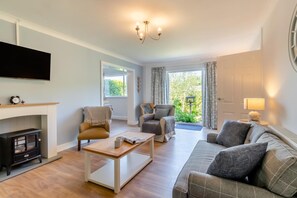 A living room with a fireplace, sofa, armchair, and television. - 3 Bed in Tenby (oc-o29381) (Tenby)