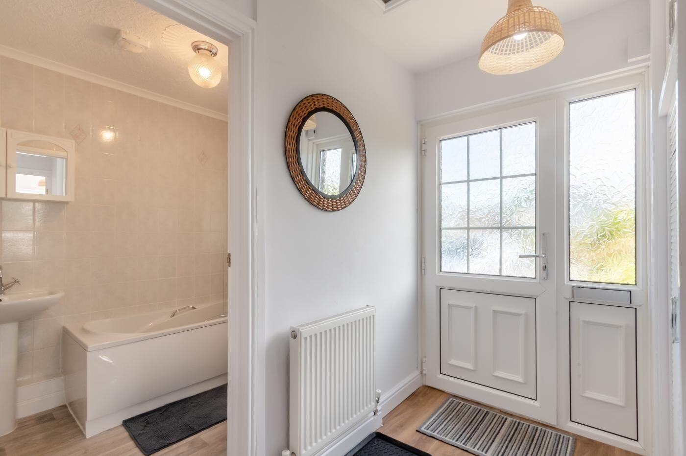 A bathroom with a bathtub, a sink, a mirror, a radiator, and a door with frosted glass windows.