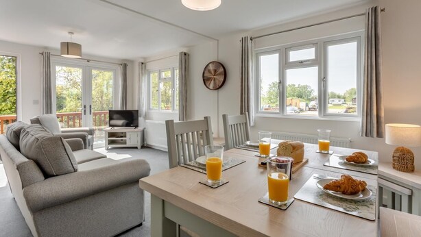 En moderne stue med sofa, TV, spisebord med morgenmad og store vinduer med udsigt.
