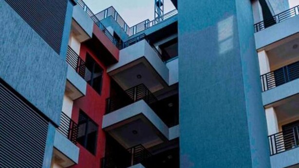 Un edificio de varios pisos con un diseño arquitectónico moderno, con balcones y una combinación de colores rojo y azul en su fachada.