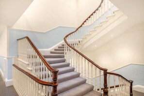 A grand staircase with a wooden handrail and white balusters, leading to a landing with a patterned wall. - 1 Bed in Buxton (oc-a29363) (Buxton)