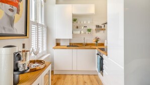Eine moderne Küche mit weißen Schränken, einer Holz Arbeitsplatte und einem eingebauten Ofen. Ein Fenster mit Jalousien, ein gerahmtes Kunstwerk an der Wand und eine Vase mit Blumen auf der Arbeitsplatte sind zu sehen.