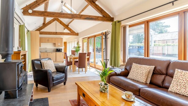 Un salon chaleureux avec une cheminée, un canapé en cuir, une table basse en bois et de grandes fenêtres donnant sur l’extérieur.