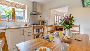 Cocina moderna con comedor, con una mesa de madera lista para el desayuno, con croissants, jugo y un jarrón de flores.