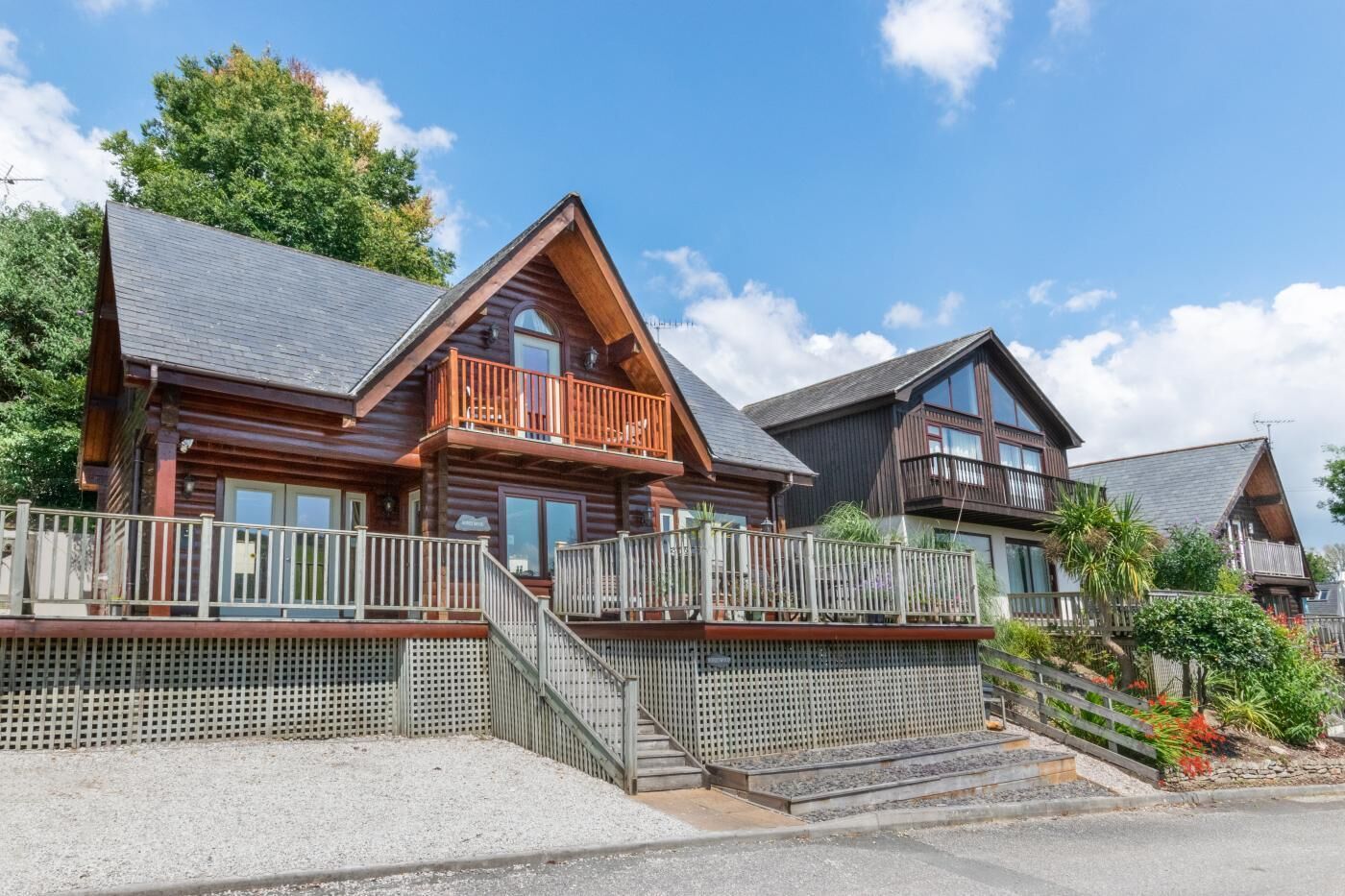 Une rangée de chalets en rondins, dotés de balcons et de rampes en bois, et bordée d’une allée en gravier.