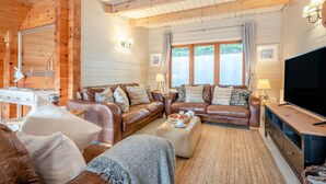 Une chambre confortable, aménagée dans le style d’un chalet, avec un grand plafond en bois, un ensemble de canapés en cuir, un téléviseur à écran plat et une table à manger agrémentée d’un panier de fruits.