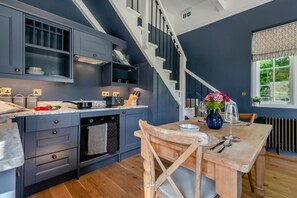 Une cuisine moderne avec des meubles de couleur bleu foncé, une table à manger en bois et un escalier.