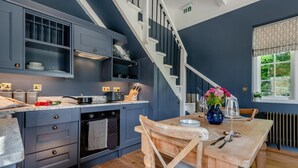 A modern kitchen with dark blue cabinets, a wooden dining table, and a staircase. - 1 Bed in Tollard Royal (oc-t29453) (Tollard Royal)