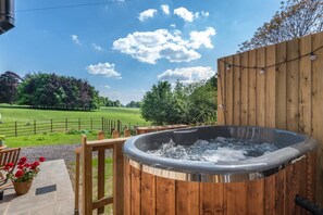 Un jacuzzi con terraza de madera y vista a un campo verde.