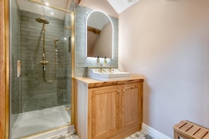 Un baño con ducha envuelta en vidrio, tocador de madera con lavamanos y un espejo sobre el tocador.