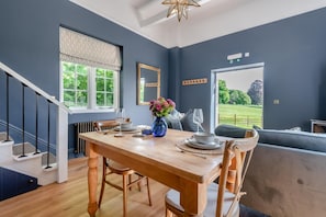 Un comedor con mesa de madera, sillas, un jarrón de flores y vistas a un paisaje verde por una ventana.