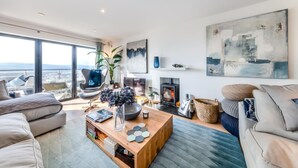 A modern living room with a large window, a fireplace, and a view of the sea. - 5 Bed in Aberdovey (oc-t29402) (Aberdovey)