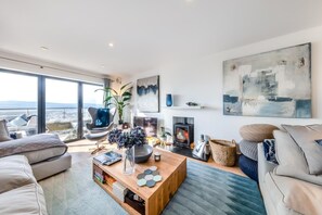 Ein modernes Wohnzimmer mit großem Fenster, Kamin und Meerblick.