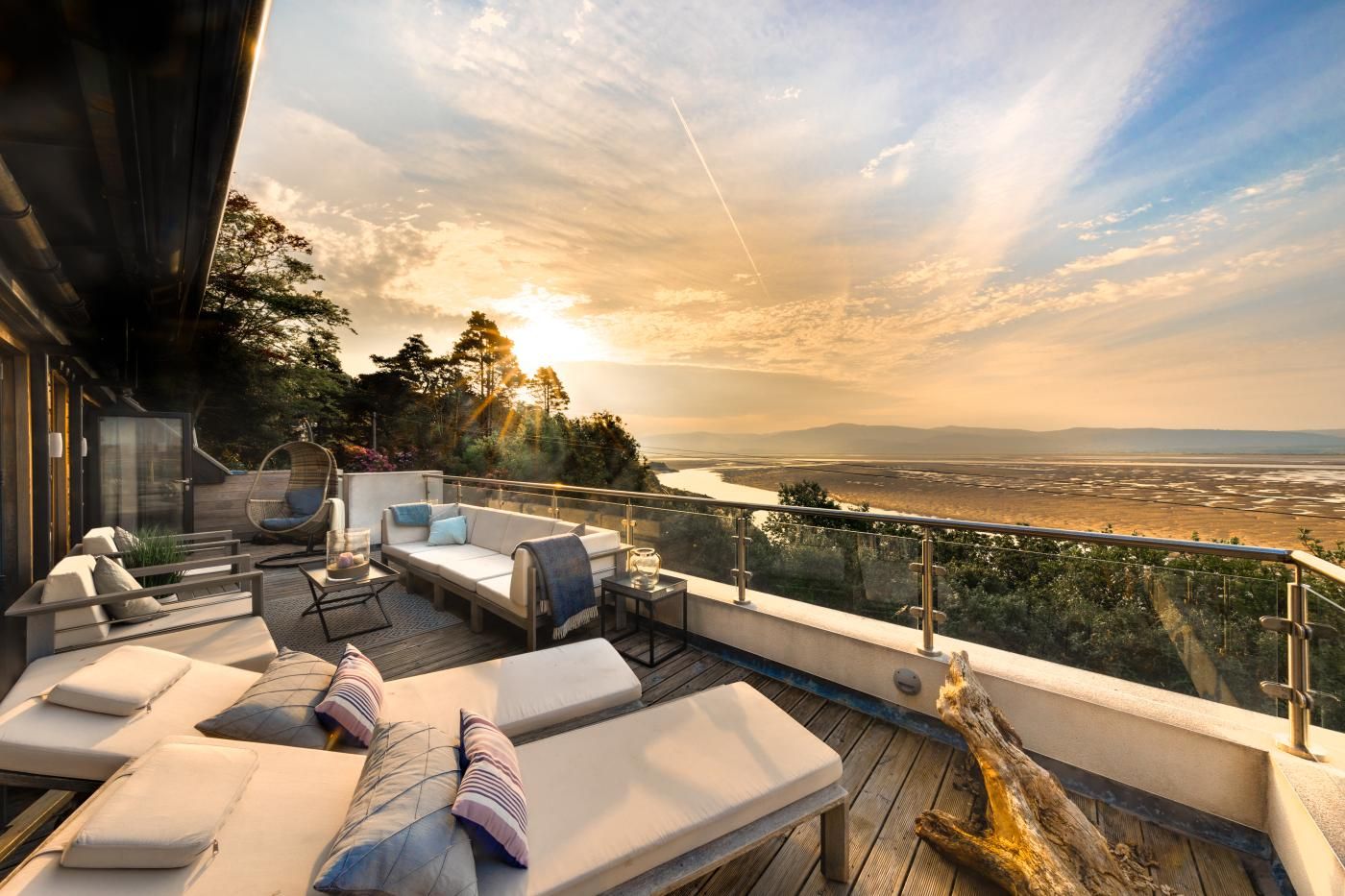 A deck with lounge chairs and a sofa, overlooking a river and distant landscape.
