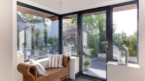 A corner room with a wicker sofa, a glass door leading outside, and a lantern on the windowsill. - 5 Bed in Aberdovey (oc-t29402) (Aberdovey)