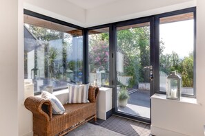 Ein Eckzimmer mit einem Korbsessel, einer Glastür, die nach draußen führt, und einer Laterne auf der Fensterbank.