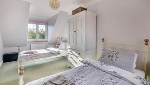 Een slaapkamer met twee bedden, een witte kledingkast en een raam met uitzicht op groen.