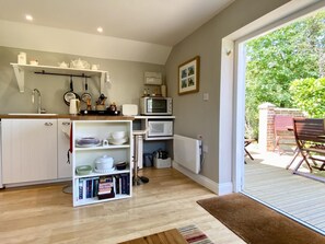 A compact kitchen with white cabinetry, a built-in bookshelf, and a dining area with outdoor seating. - 1 Bed in Cratfield (oc-t29434) (Cratfield)