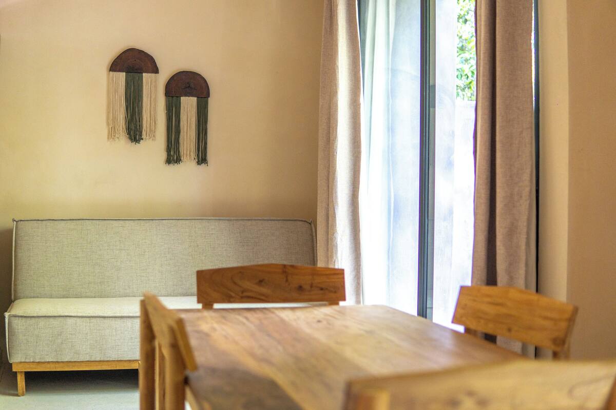 Um quarto com uma mesa de jantar de madeira, um sofá bege e uma janela com cortinas.